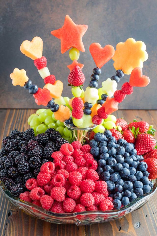 A heaping fruit tray with piles of blackberries, raspberries, blueberries, strawberries and green grapes, and a fruit bouquet at its center