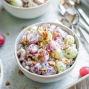 One small serving bowl of grape salad, on a serving tray with spoons and other small bowls in the background