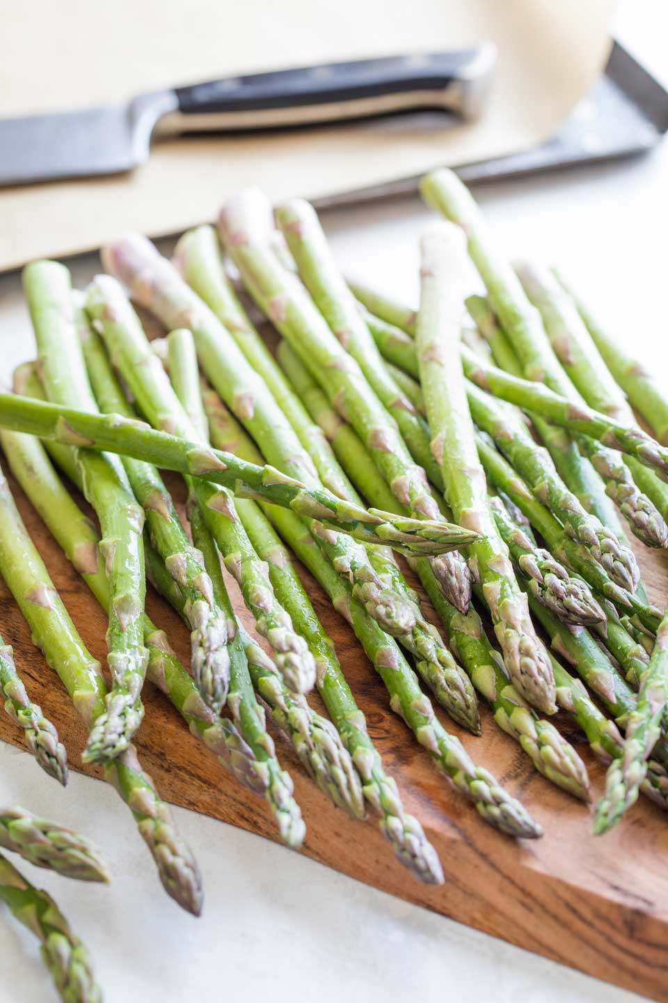 Pencil-width asparagus spears that are fresh and damp with water droplets, spilled across a cutting board.