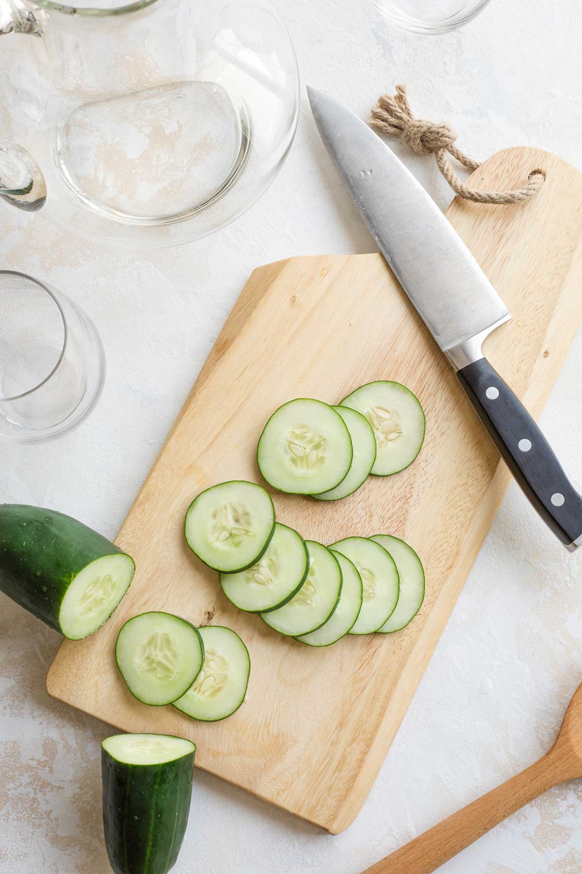 Overhead of a cucumber and slices on a cutting board with a black-handled knife.