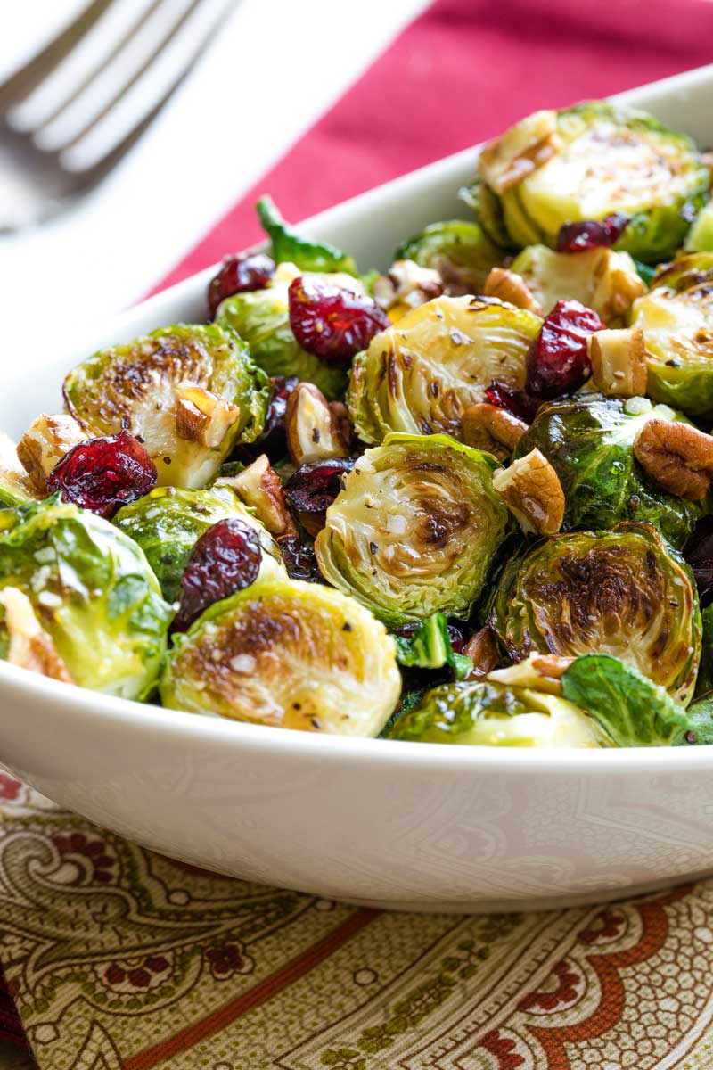 Closeup of one end of white serving dish piled with roasted Brussels sprouts on top of patterned napkin.