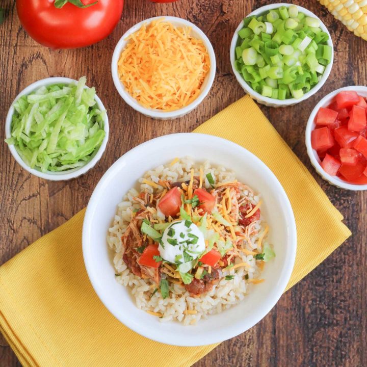 Large white dish filled with finished burrito bowl recipe and surrounded by smaller white cups of toppings.